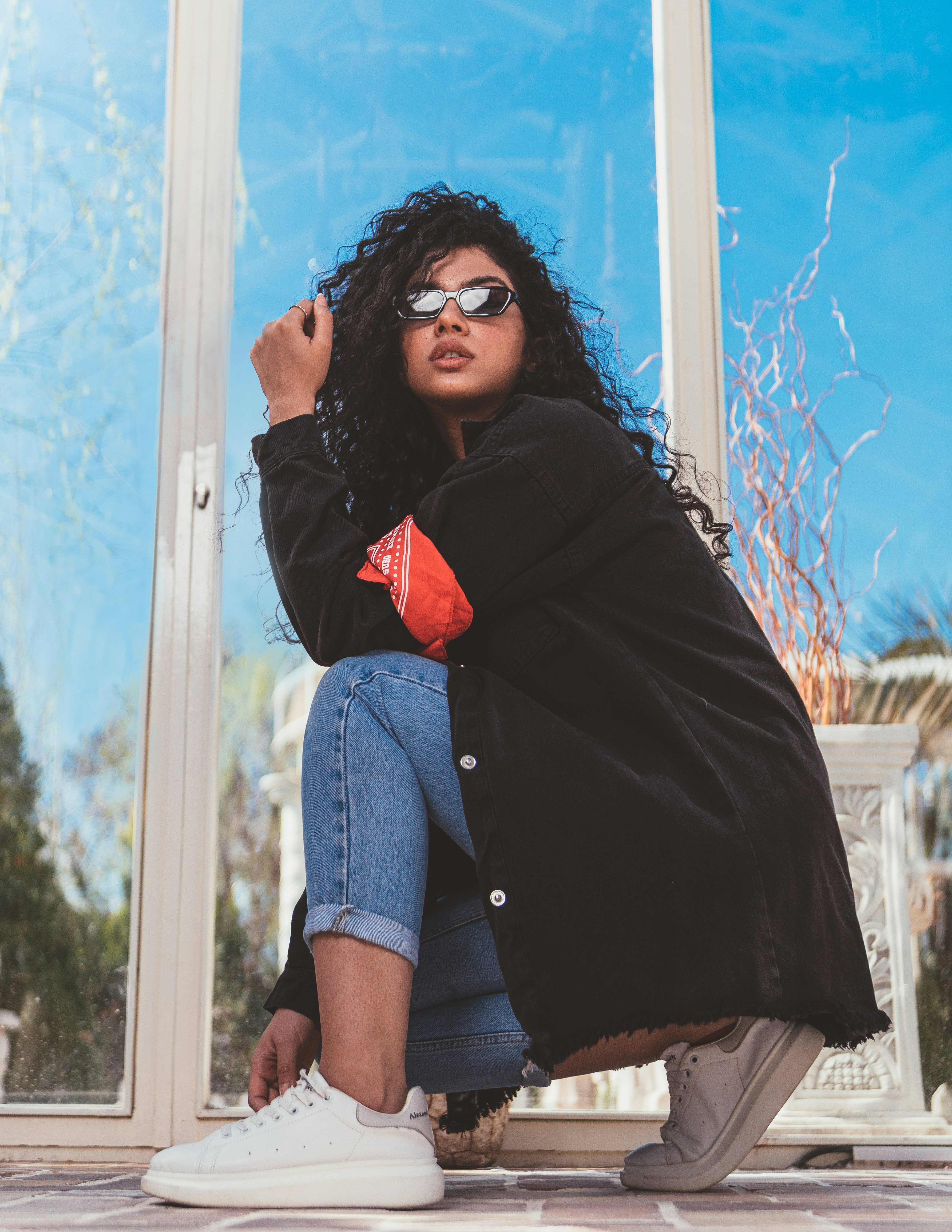 woman in black coat and blue denim shorts standing beside glass window